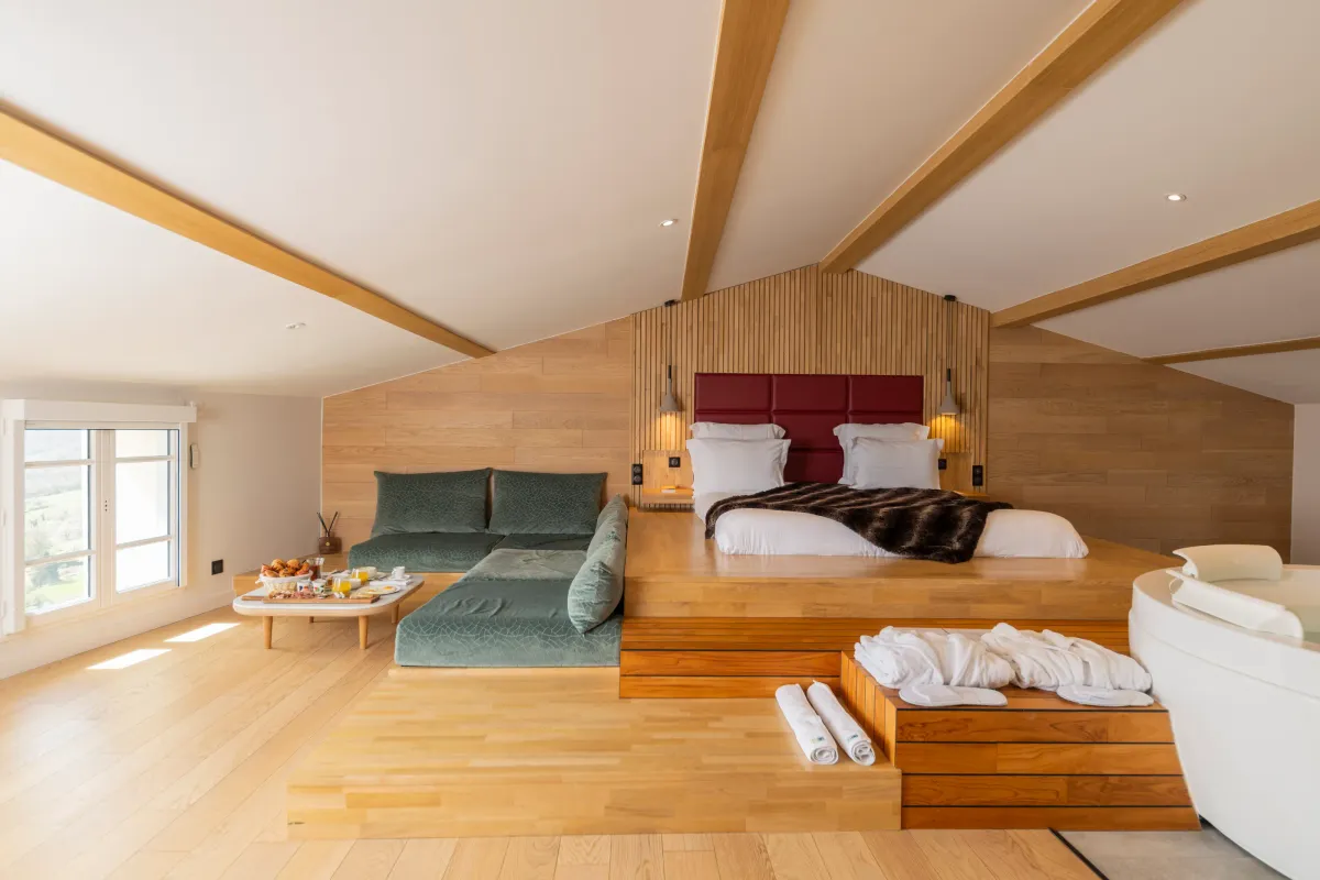 Spacious room with elevated main bed, sofa, coffee table with food and drinks, and windows offering an outdoor view.