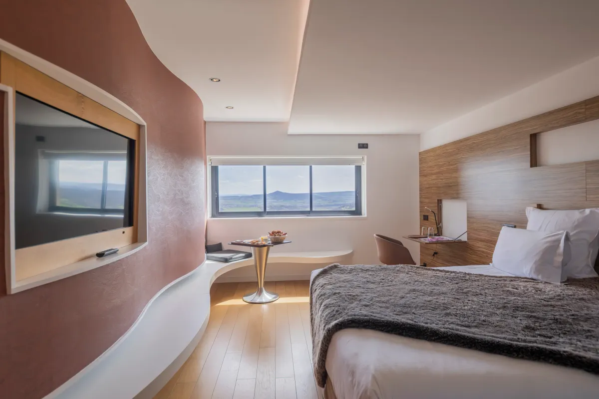 Chambre moderne avec lit, télévision, table avec fruits et vue panoramique sur le paysage extérieur