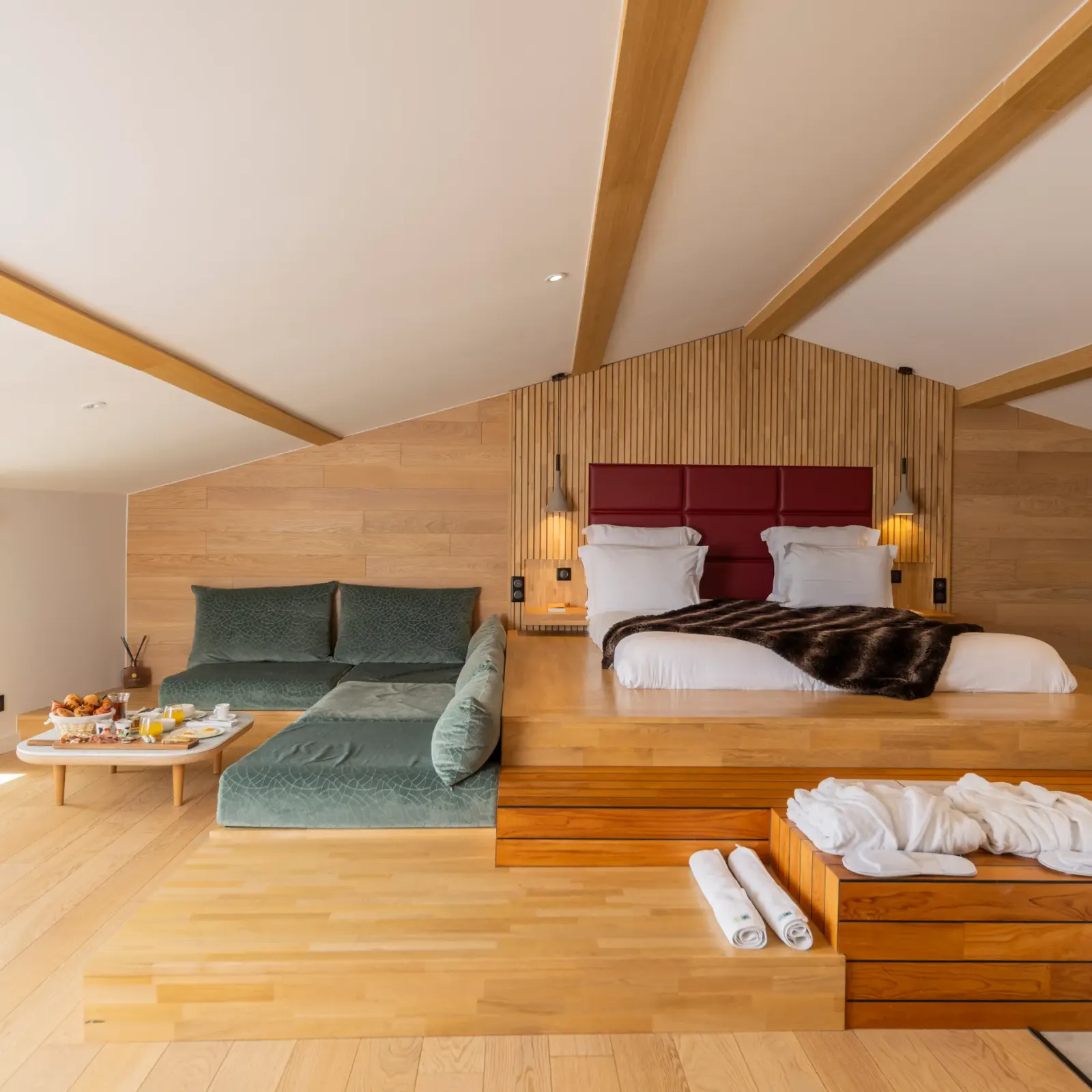 Chambre spacieuse avec lit principal surélevé, canapé, table basse avec nourriture et boissons, et fenêtres offrant une vue extérieure