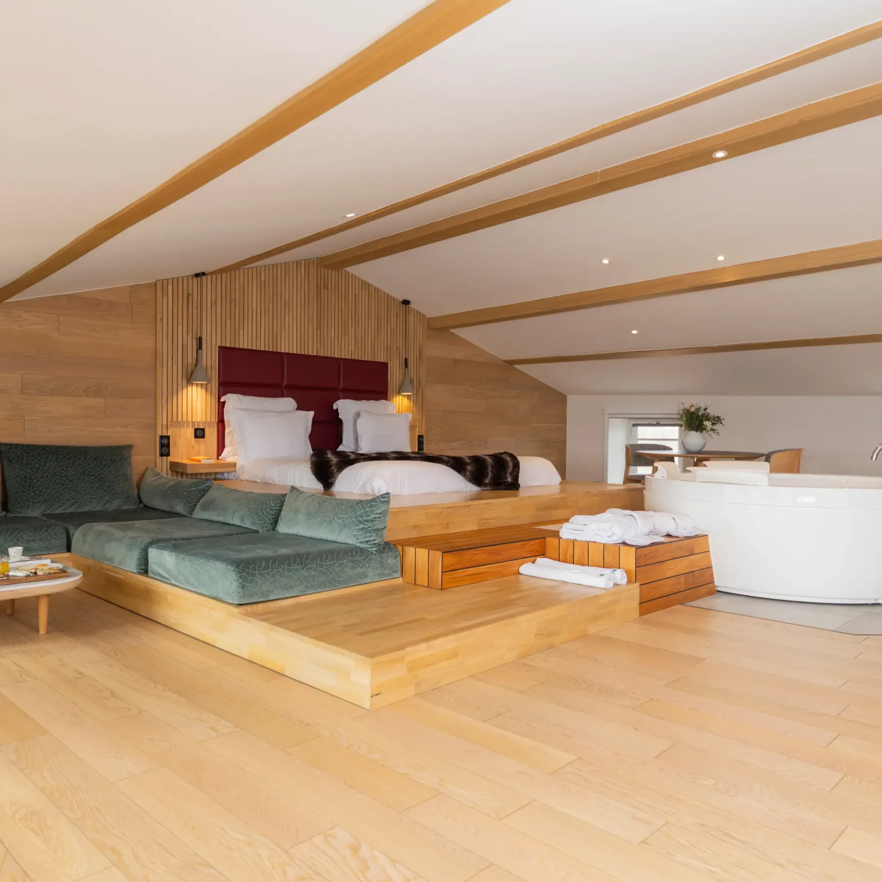 Chambre spacieuse avec lit surélevé, canapé vert, table basse avec nourriture, et baignoire blanche près d'une fenêtre