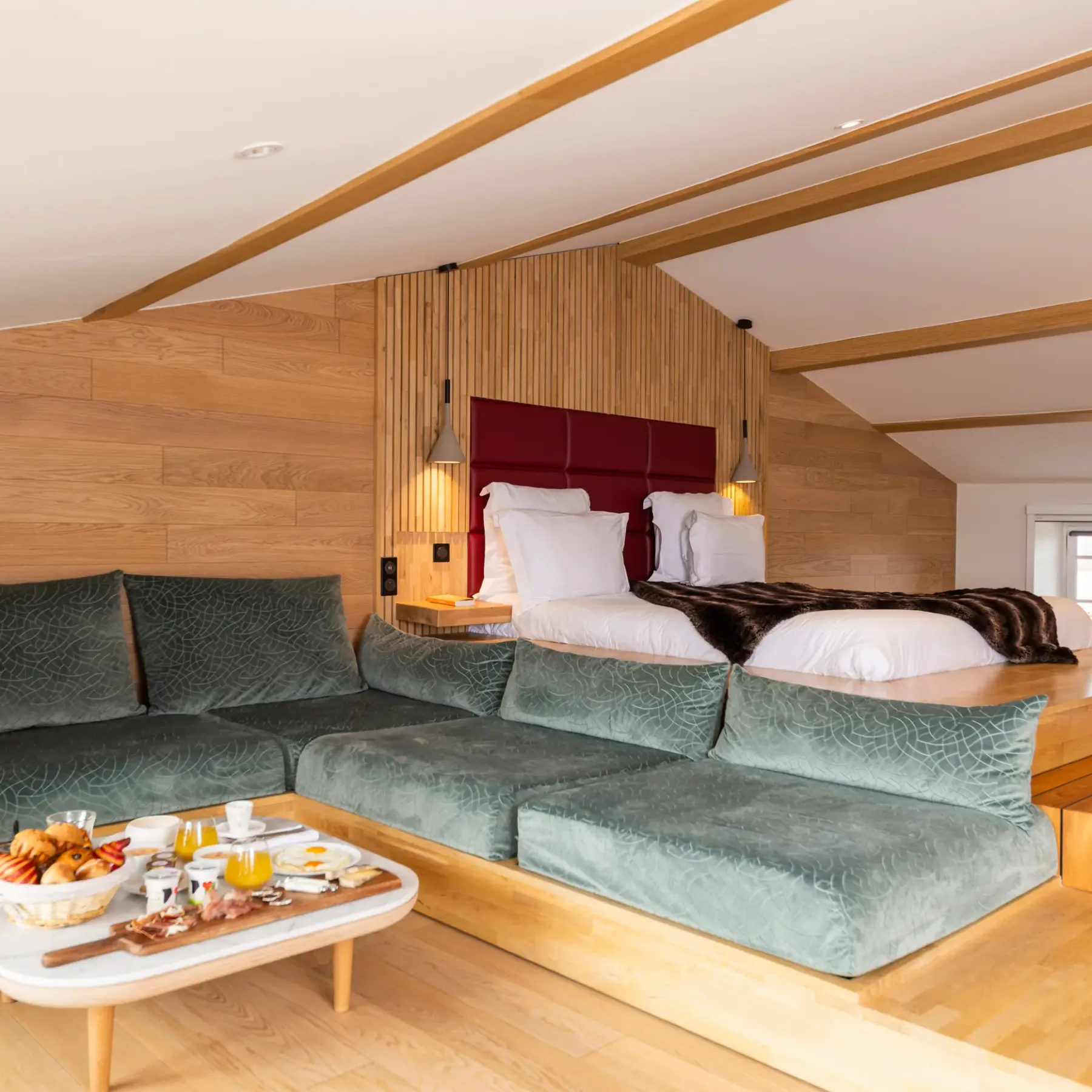 Chambre avec lit double et canapé vert, table basse avec plateau de petit-déjeuner, murs en bois et plafond incliné