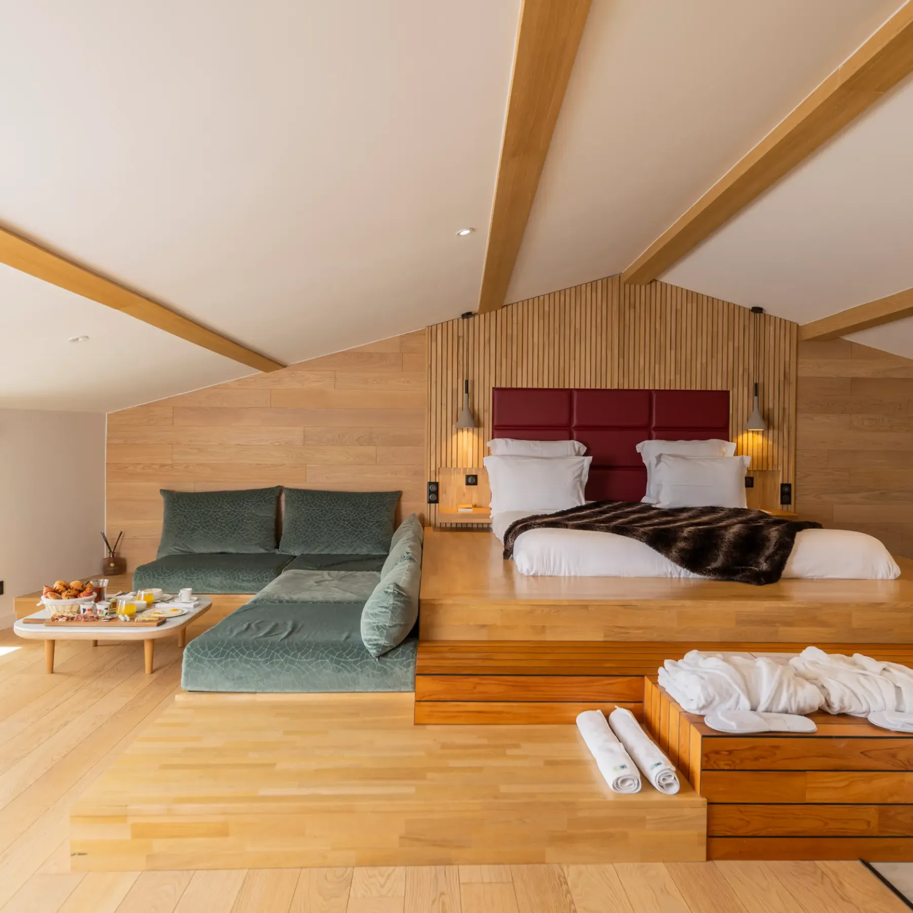 Chambre spacieuse avec lit principal surélevé, canapé, table basse avec nourriture et boissons, et fenêtres offrant une vue extérieure