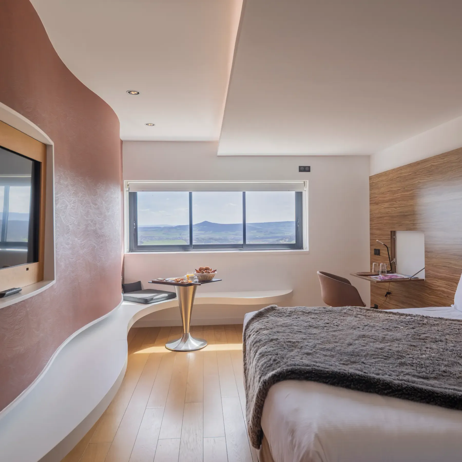 Chambre moderne avec lit, télévision, table avec fruits et vue panoramique sur le paysage extérieur