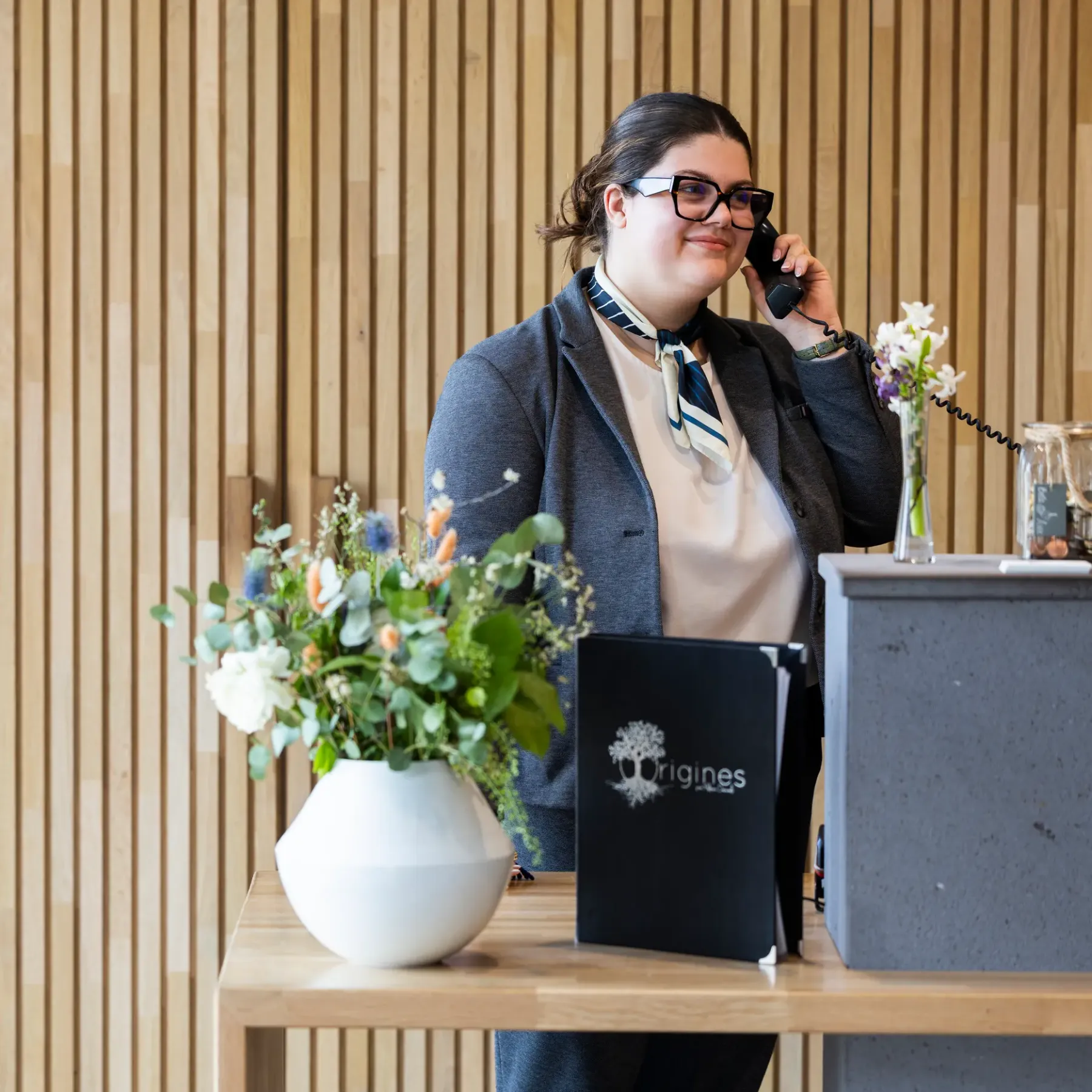 Une personne au téléphone derrière un comptoir avec un vase de fleurs et un livre noir