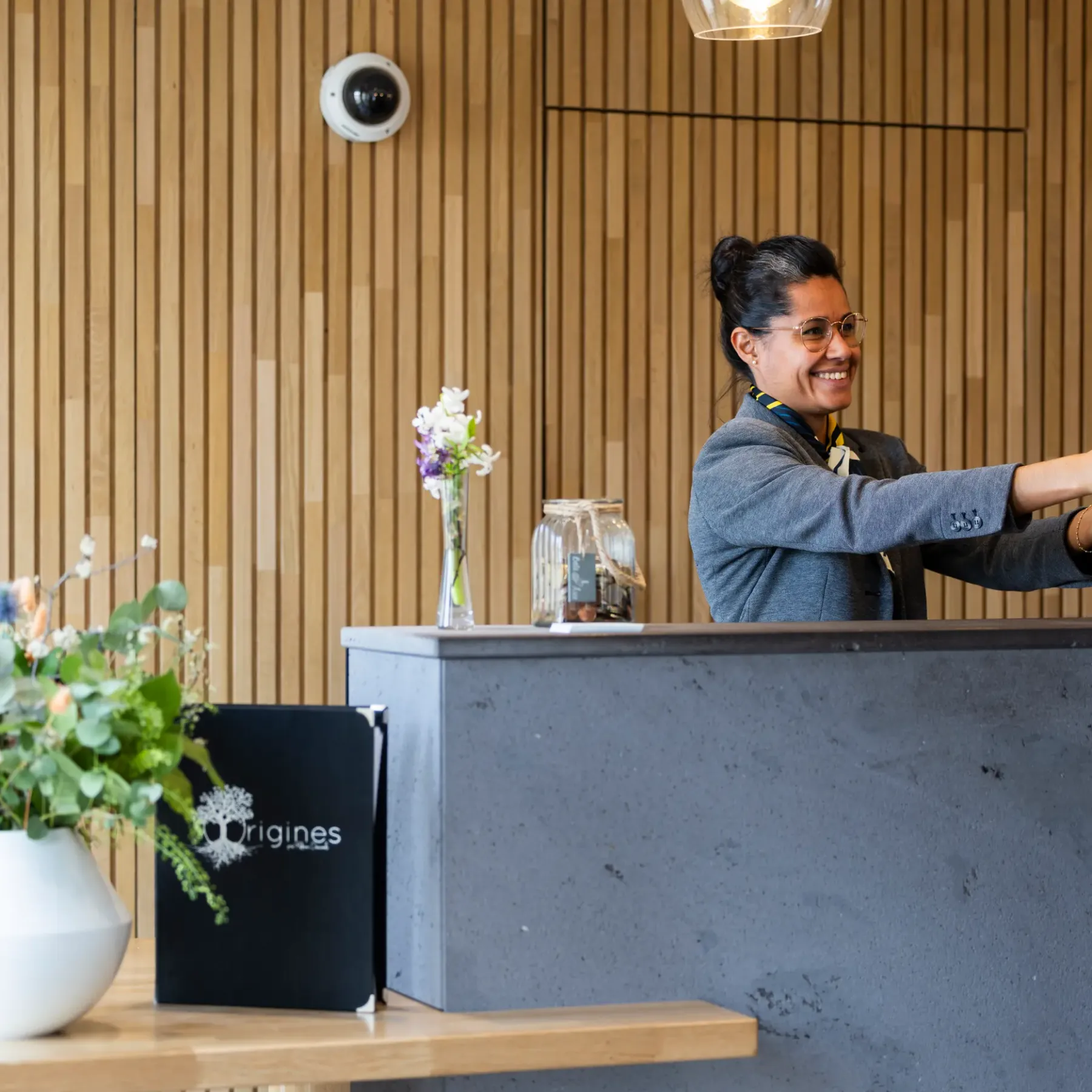 Une personne derrière un comptoir remet une carte à un client dans un espace intérieur avec des murs en bois et des fleurs