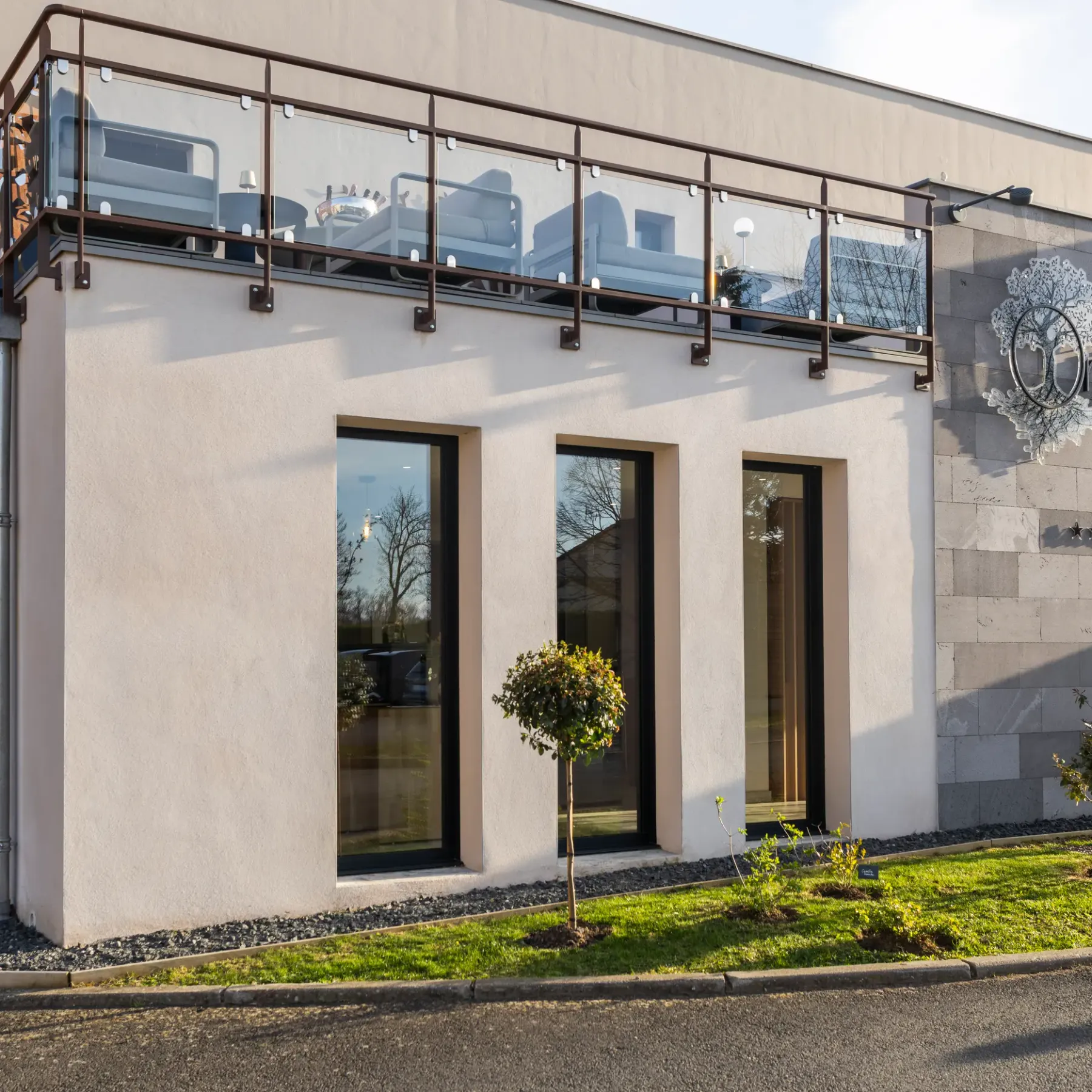 Bâtiment moderne avec une façade en pierre et en stuc, une porte vitrée et un balcon à la rambarde métallique, arborant le nom "Origines"