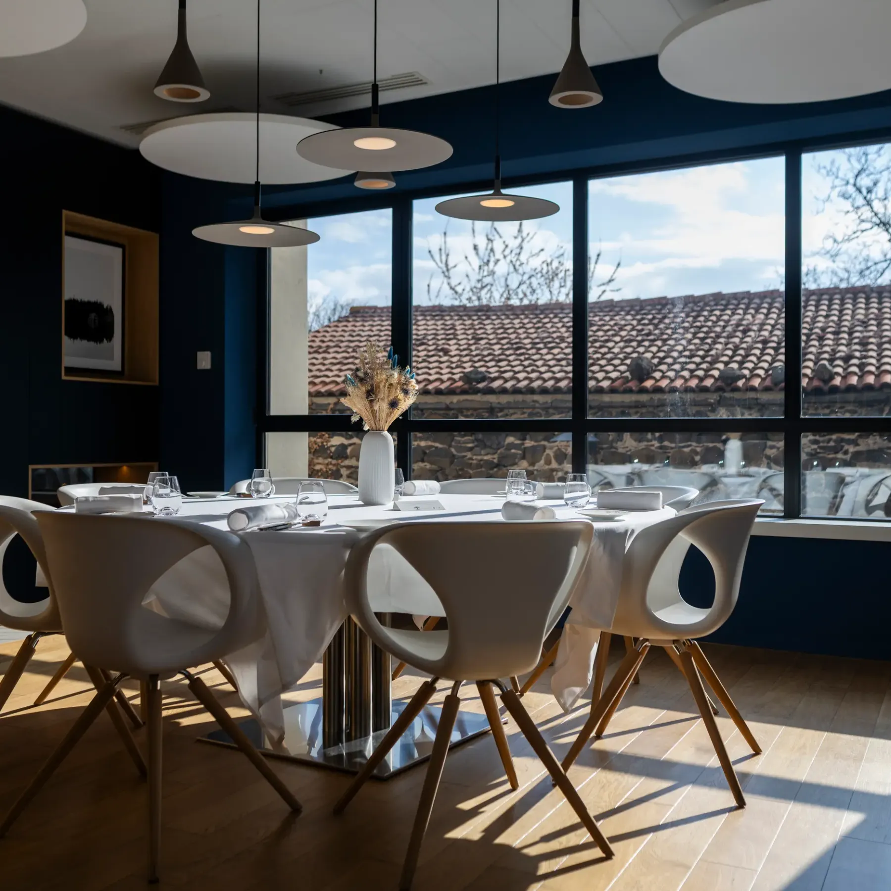 Une table ronde avec des chaises modernes devant une grande fenêtre donnant sur un toit en tuiles