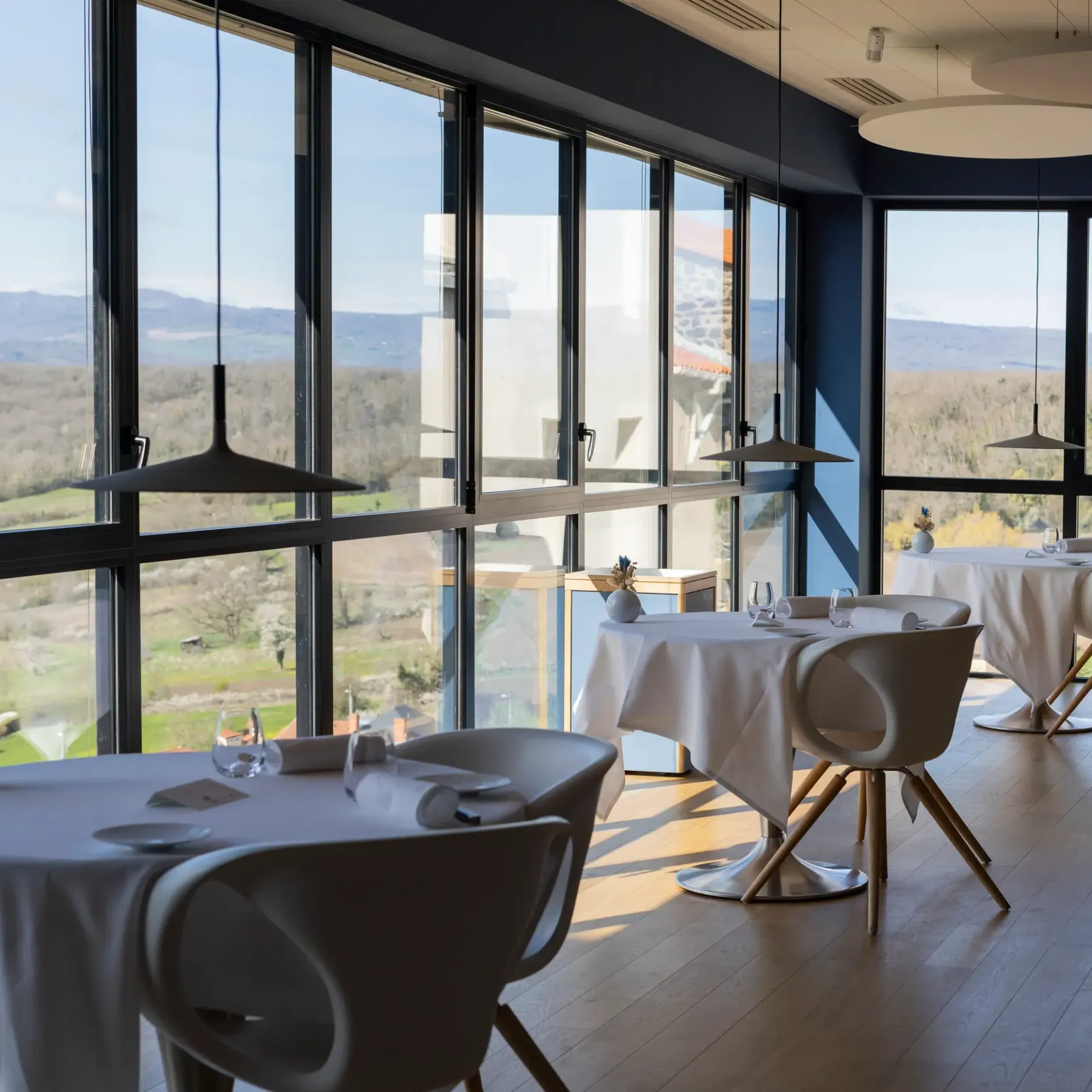 Salle de restaurant avec tables et chaises modernes, vue panoramique sur un paysage vallonné à travers de grandes baies vitrées