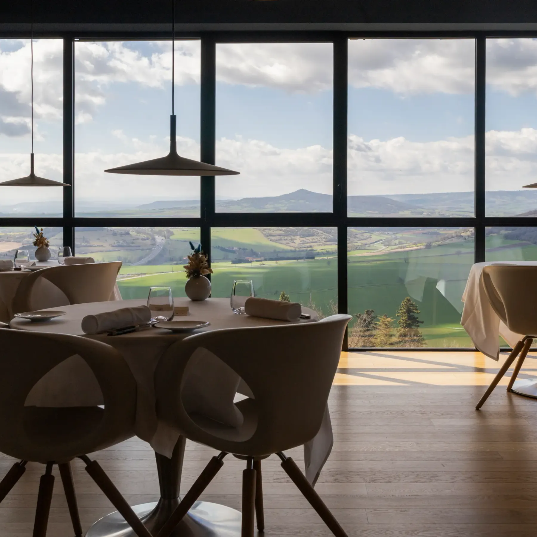 Une salle à manger avec une grande baie vitrée offrant une vue sur un paysage vallonné et des montagnes au loin