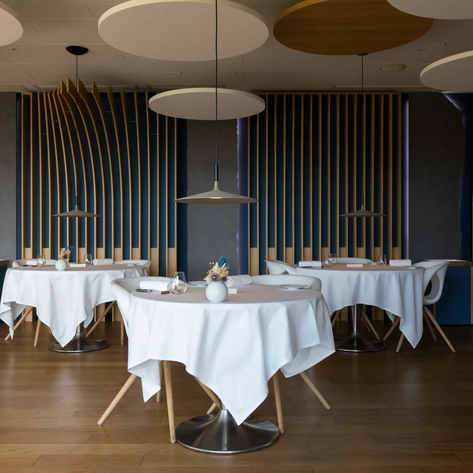 Salle de restaurant avec tables rondes recouvertes de nappes blanches, chaises modernes et luminaires suspendus