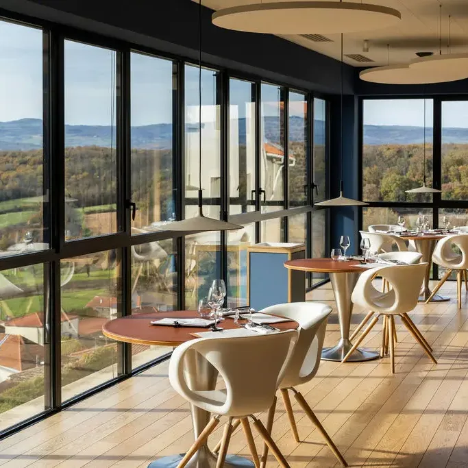 Restaurant room with large windows offering a view of a rural landscape and round tables with modern chairs.