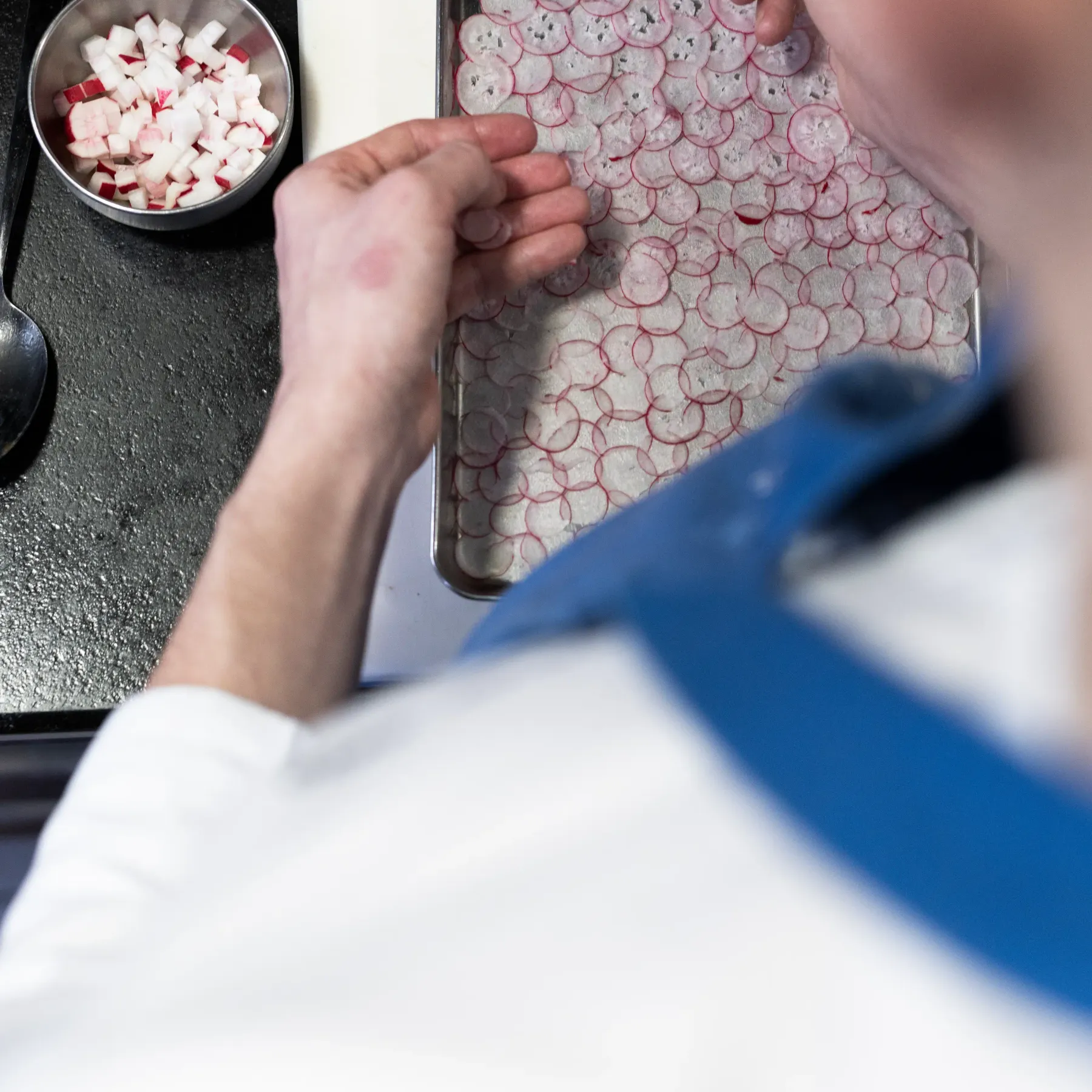 Une personne découpe des rondelles de radis et les dispose sur une plaque de cuisson