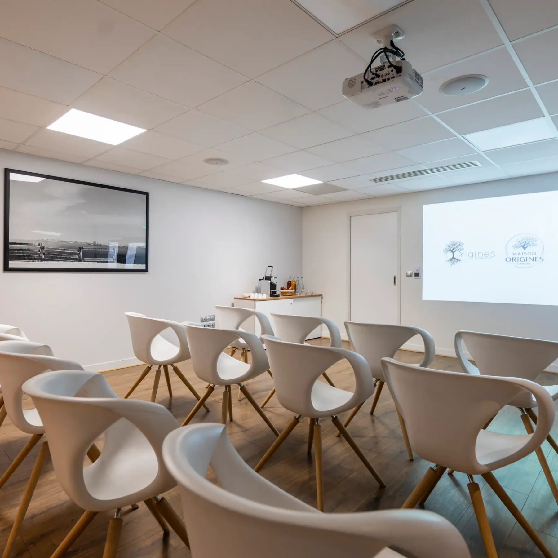 Salle de réunion avec des chaises disposées en cercle, un projecteur et un écran affichant des logos