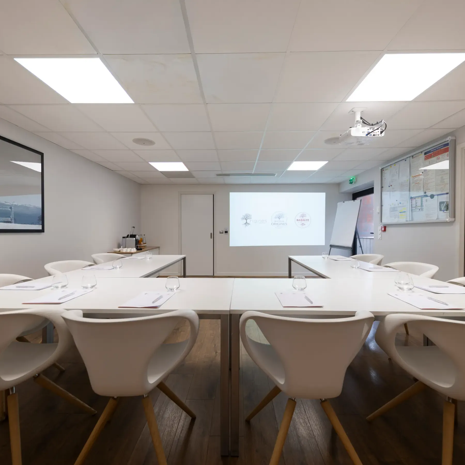 Salle de réunion avec table ovale, chaises blanches et projecteur affichant des logos sur un écran