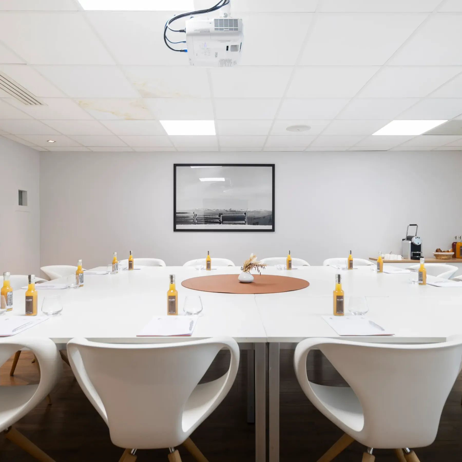 Salle de réunion avec une table ronde, des chaises blanches, des bouteilles d'eau et un projecteur au plafond