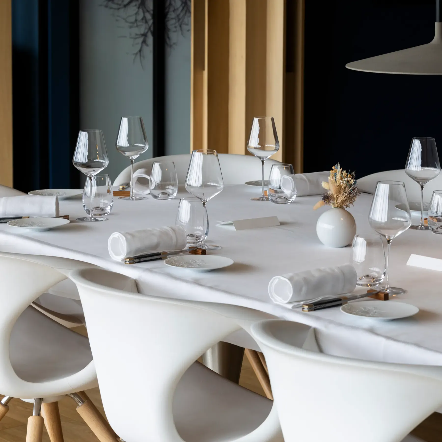Table ronde blanche avec des verres à vin, des serviettes et des couverts, entourée de chaises modernes dans un intérieur élégant