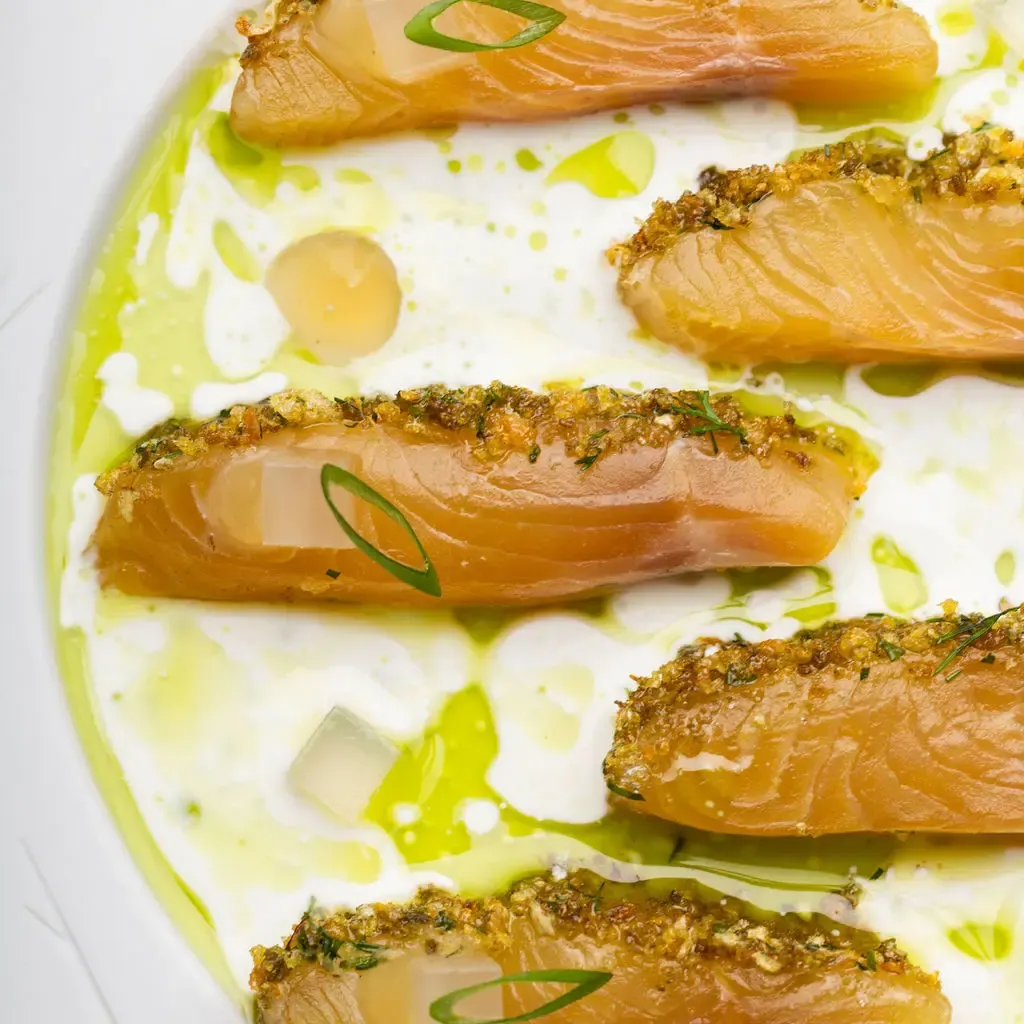 Quatre filets de poisson garnis d'herbes et de panko, disposés sur une sauce verte et blanche dans une assiette blanche