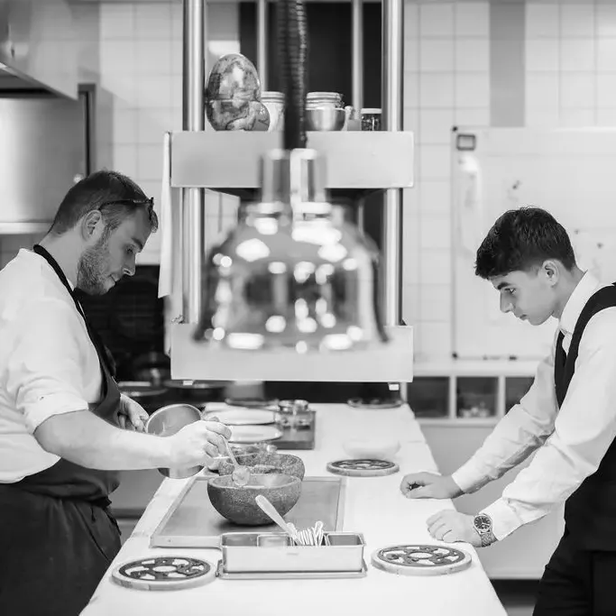 Deux personnes en tenue professionnelle préparent des plats dans une cuisine équipée de matériel de restauration