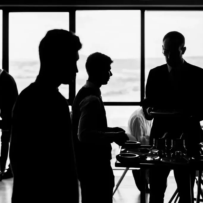 Quatre personnes en silhouette discutent autour d'une table avec des tasses, devant une grande fenêtre offrant une vue sur l'extérieur