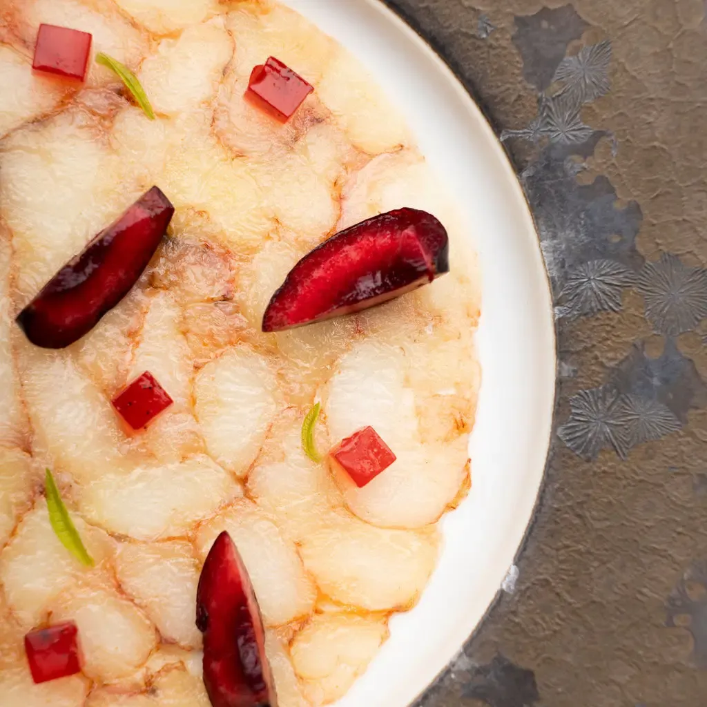 A white dish containing plantain chips with pieces of chili and tomato, placed on a patterned metal surface.