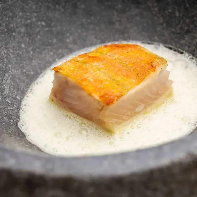 Un morceau de poisson poché dans un liquide blanc, présenté dans une poêle en fonte