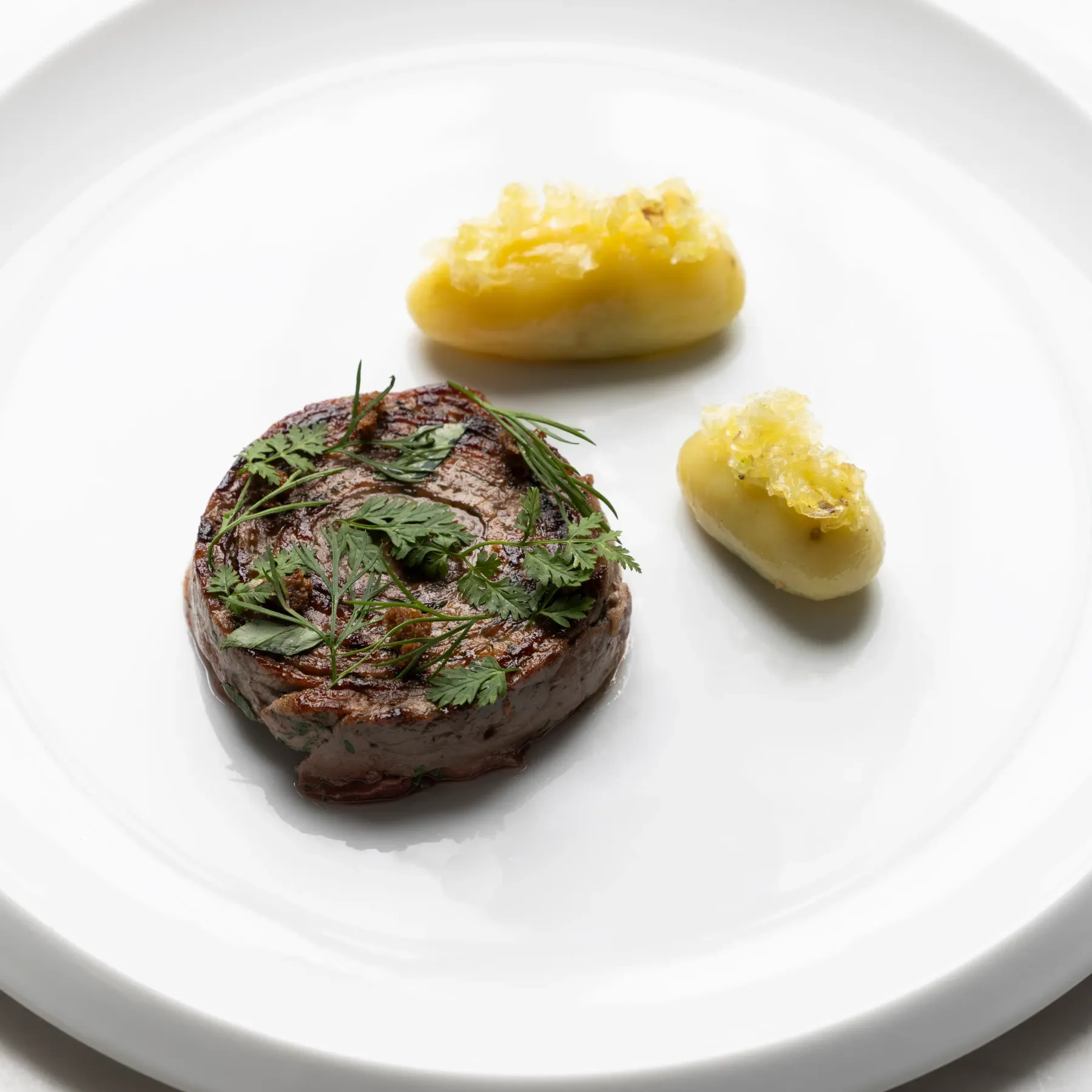 Un steak grillé garni de persil et deux pommes de terre rissolées sur une assiette blanche