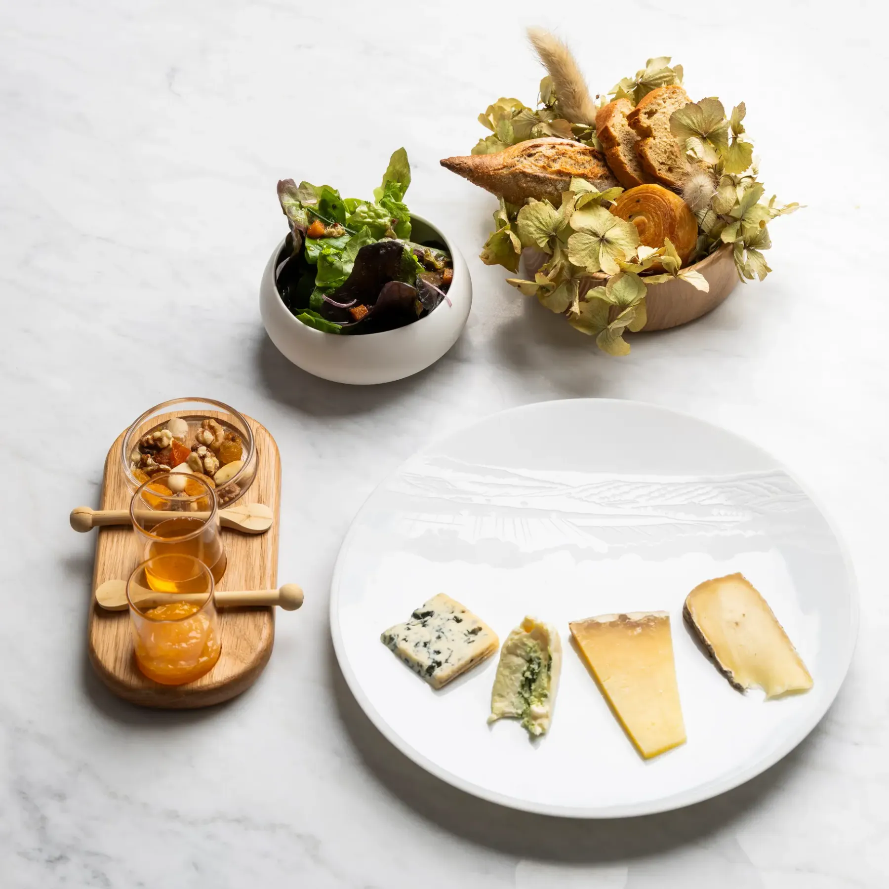 Assiette de fromages avec des accompagnements, salade et pain sur une table en marbre