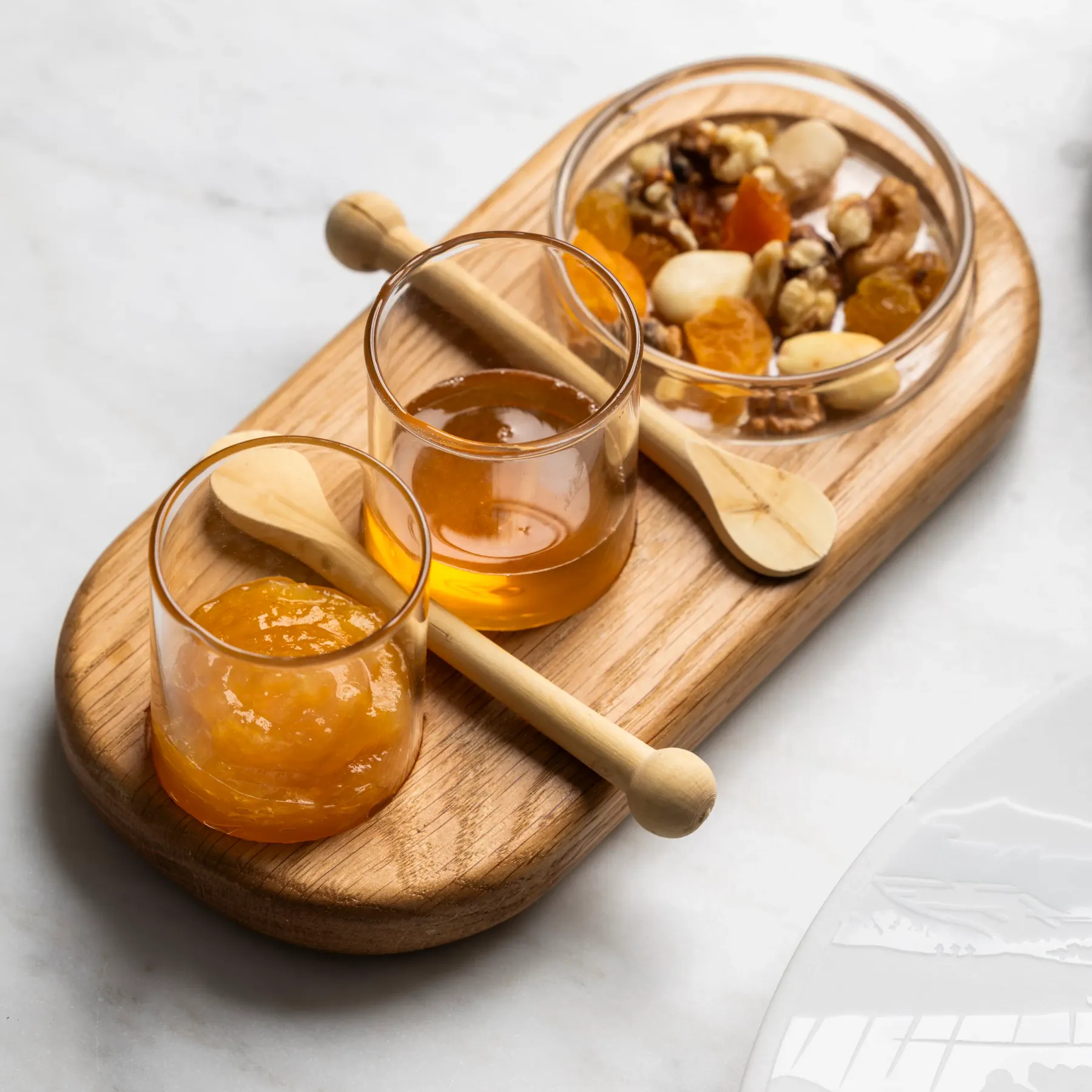 Un plateau en bois avec des petits pots de confiture, des verres de miel et un bol de noix et fruits secs