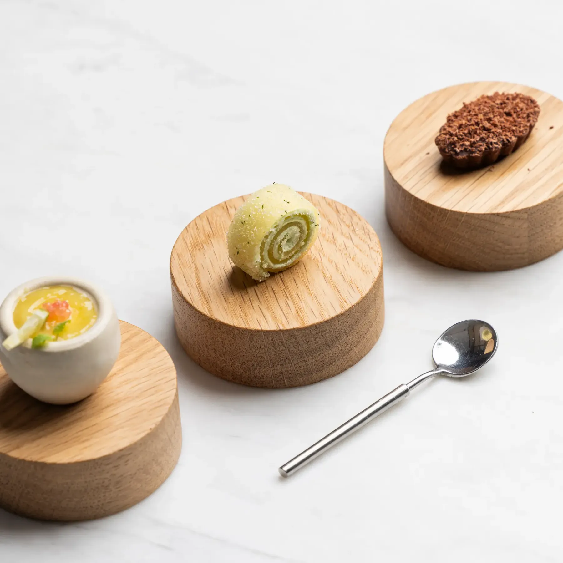 Trois petites portions de nourriture sur des supports en bois avec une cuillère à côté