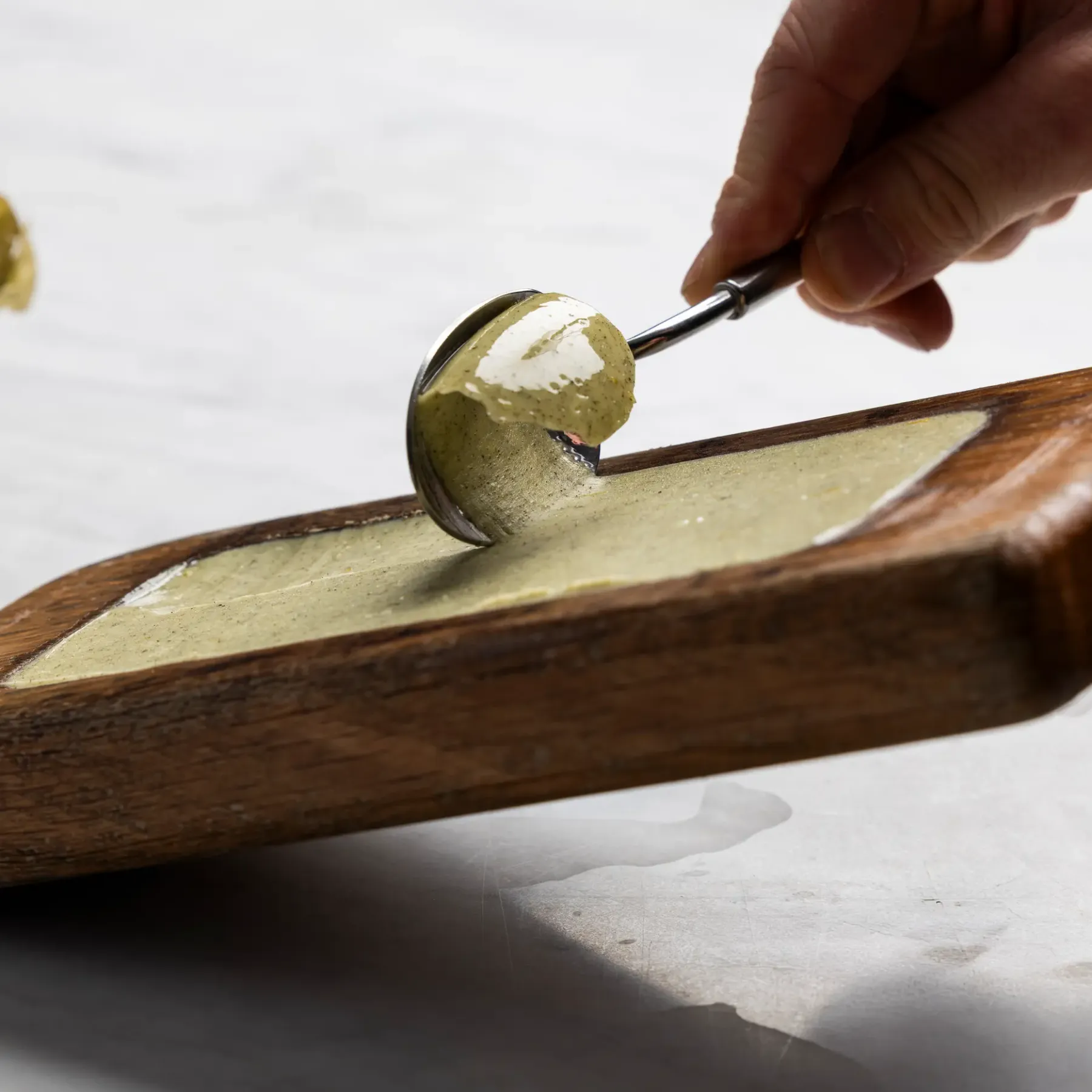 Une main étale une pâte verte sur une planche en bois à l'aide d'une spatule