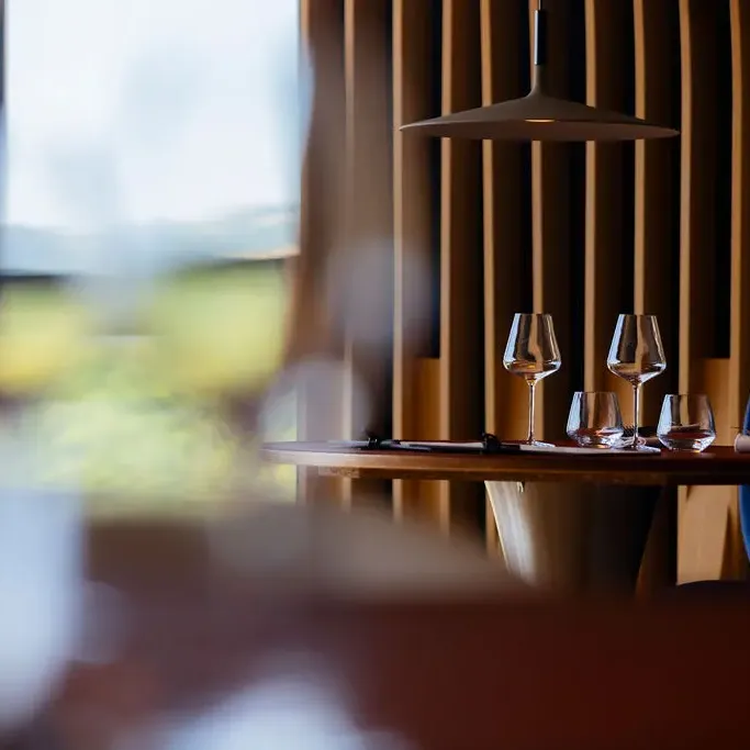 Table with four wine glasses and two cutlery sets, seen through a window with vertical blinds