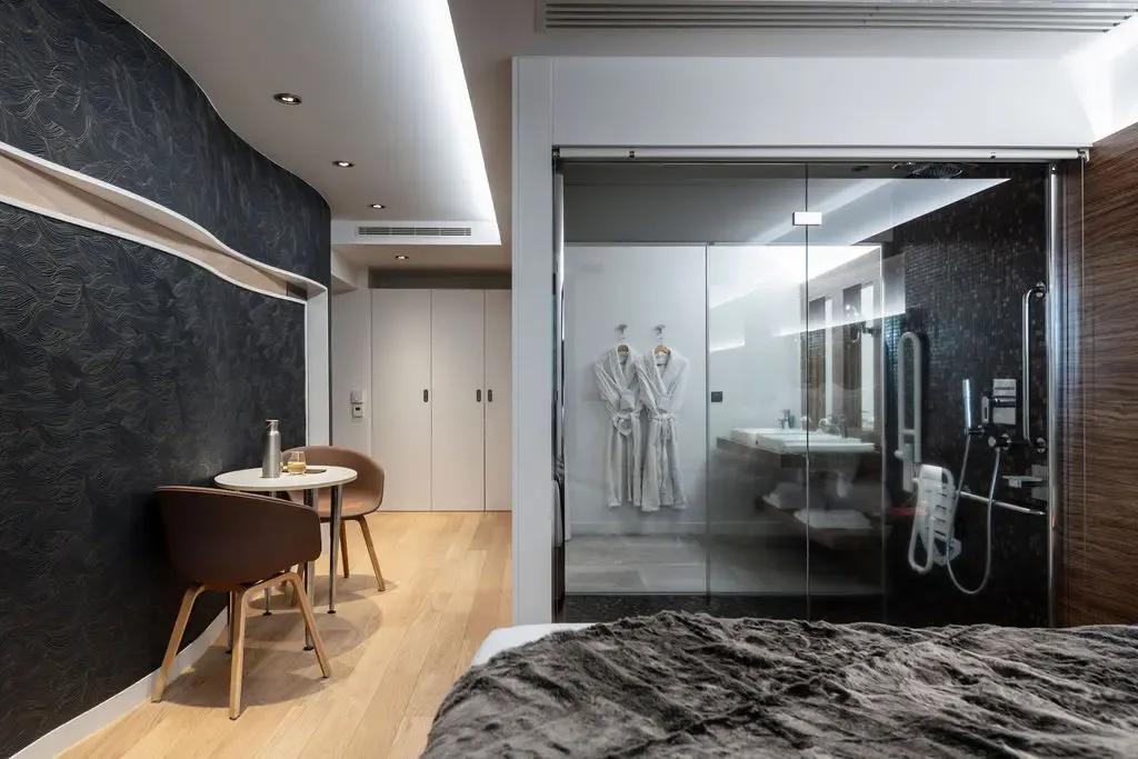 Chambre moderne avec lit, table et chaises, et salle de bain ouverte avec douche et lavabo