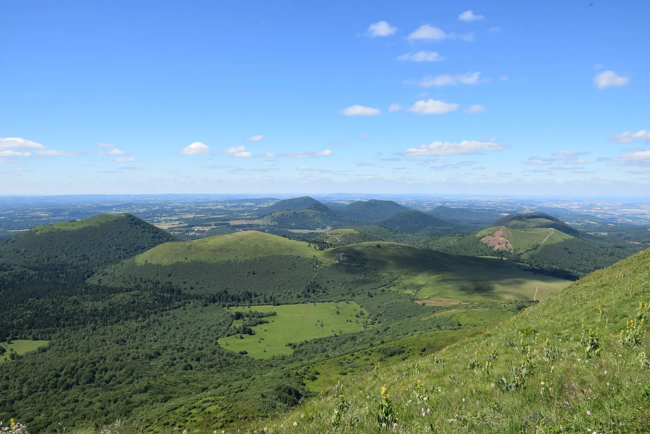 Vaste paysage de collines verdoyantes sous un ciel bleu parsemé de nuages